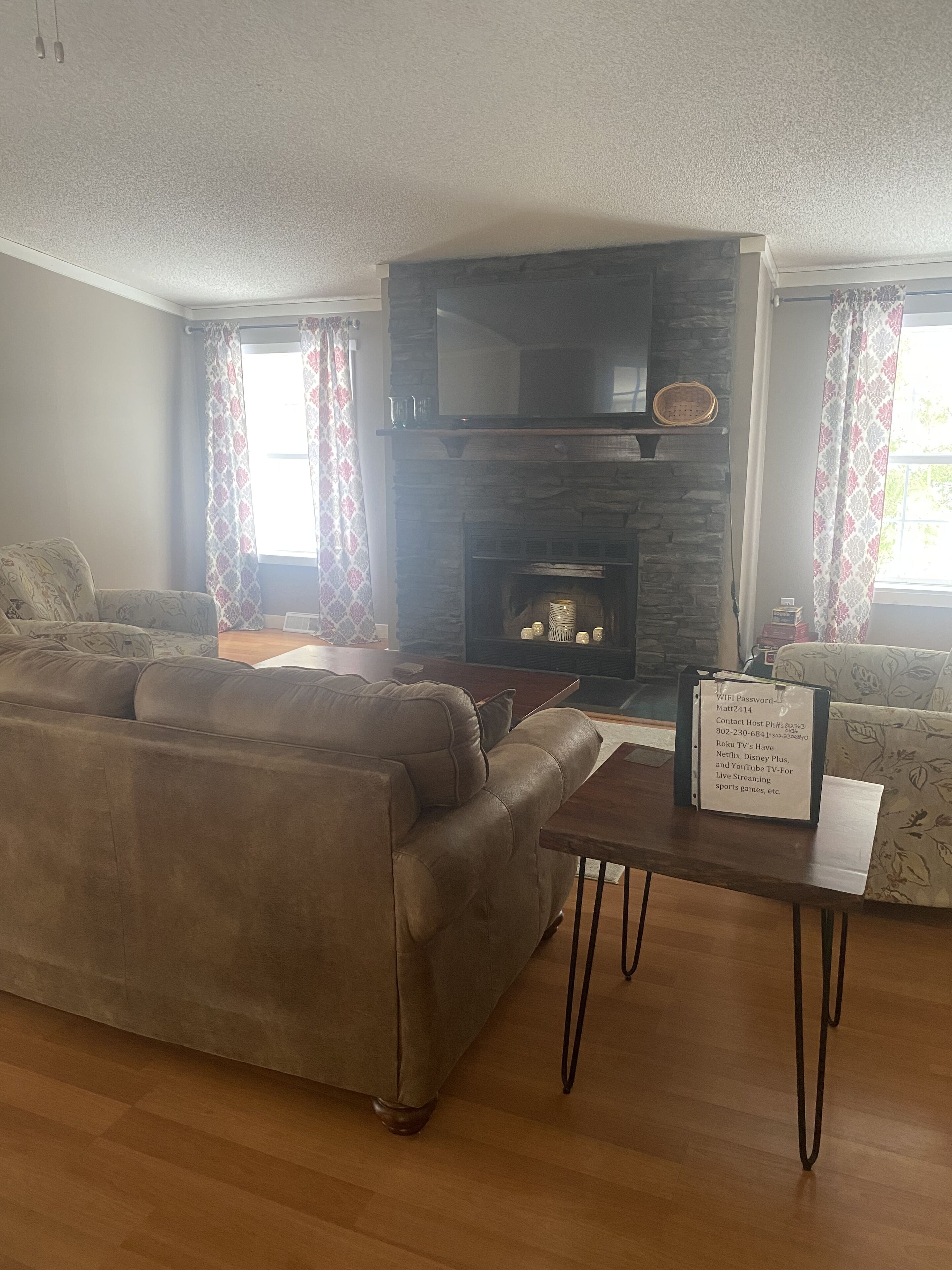 A living room with a stone fireplace, a sofa, a coffee table, and a TV mounted above the fireplace.