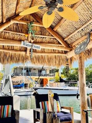 Olki- tai ruohokatteinen rakennelma, jonka kyltissä lukee ”Waterfront”, ja josta on näkymä venelaituriin sekä oleskelualue, jossa on raidallisia tyynyjä.