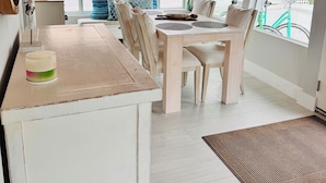 Un comedor con una mesa y sillas de madera, una lámpara colgante y ventanas amplias con vistas a zonas verdes.