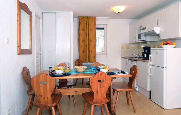 Cocina compacta con armarios blancos, un microondas y una cafetera. Hay una mesa de comedor con sillas de madera y una ventana con cortinas amarillas.