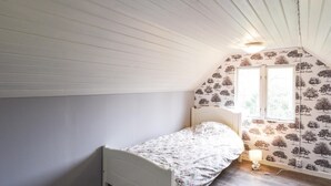 A small, single-bed room with a sloped ceiling, a window with a view of trees, and a wall with a tree pattern. - 3 bEdroom cozy home in Ed (Ed)