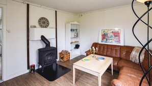 A cozy living room with a brown leather sofa, a small wooden table, a white bookshelf, and a black wood stove. - 3 bEdroom cozy home in Ed (Ed)