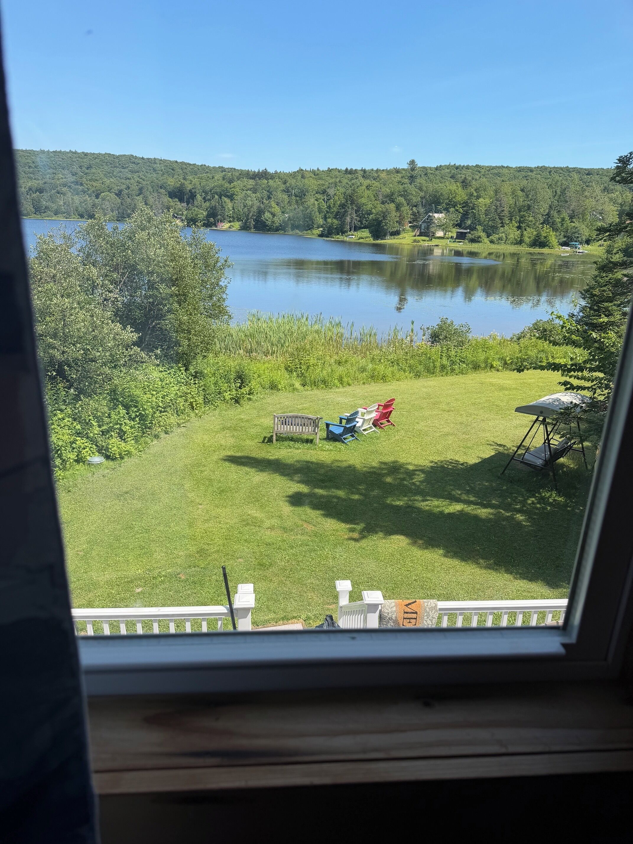 A view of a lake from a window, with a grassy area in the foreground and a forested hill in the background.