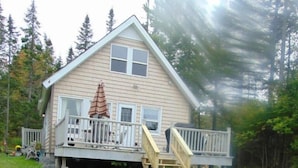 A two-story house with a deck, surrounded by a grassy yard and trees.