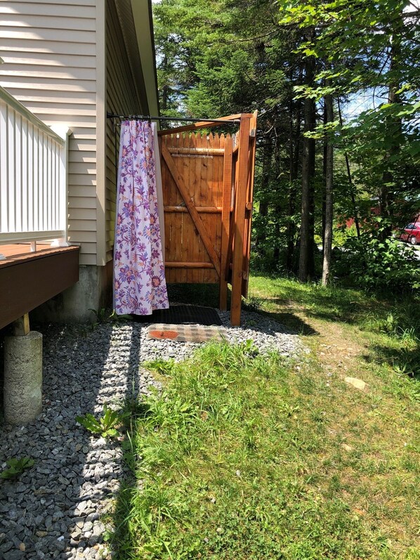 Een houten poort die uitkomt op een grindpad met een houten terras en een huis op de achtergrond.