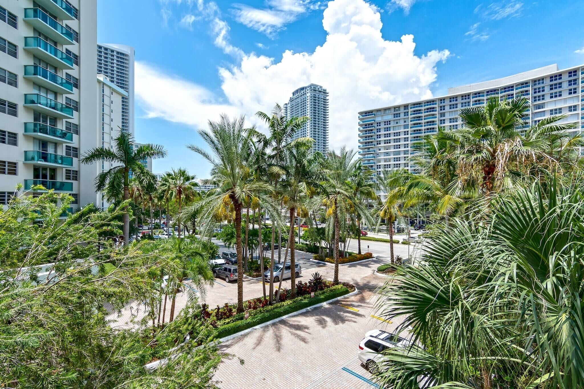 A high-rise hotel with multiple floors, palm trees, and a parking area.