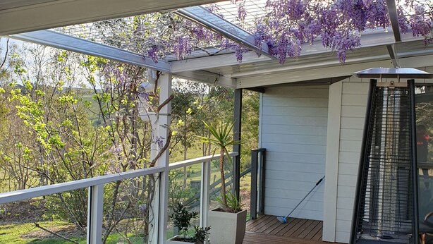 Une terrasse couverte avec une pergola, des plantes en pot, un barbecue et une chaise blanche.