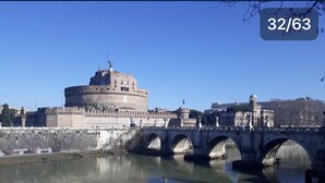 A historic stone bridge with arches spanning a calm river, leading to a large round fortress-like building with a flag on top. - View of Castel Sant'Angelo (Roma)