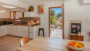 A modern kitchen with white cabinets, a wooden countertop, and a dining area with a table and chairs. There is a bowl of fruit on the table and a poster on the wall. - Nice home in Feliceto (Feliceto)