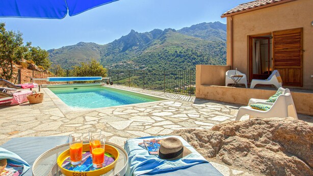 A pool area with lounge chairs, a table with drinks, and a mountain view. - Nice home in Feliceto (Feliceto)