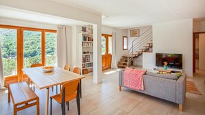 A spacious living area with a dining table, chairs, a sofa, a bookshelf, and a staircase leading to another level. - Nice home in Feliceto (Feliceto)
