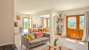 A spacious living room with a grey sofa, wooden coffee table, and a view of a mountainous landscape through large windows. - Nice home in Feliceto (Feliceto)