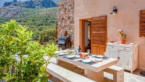An outdoor dining area with a stone wall and wooden shutters, overlooking a mountainous landscape. - Nice home in Feliceto (Feliceto)