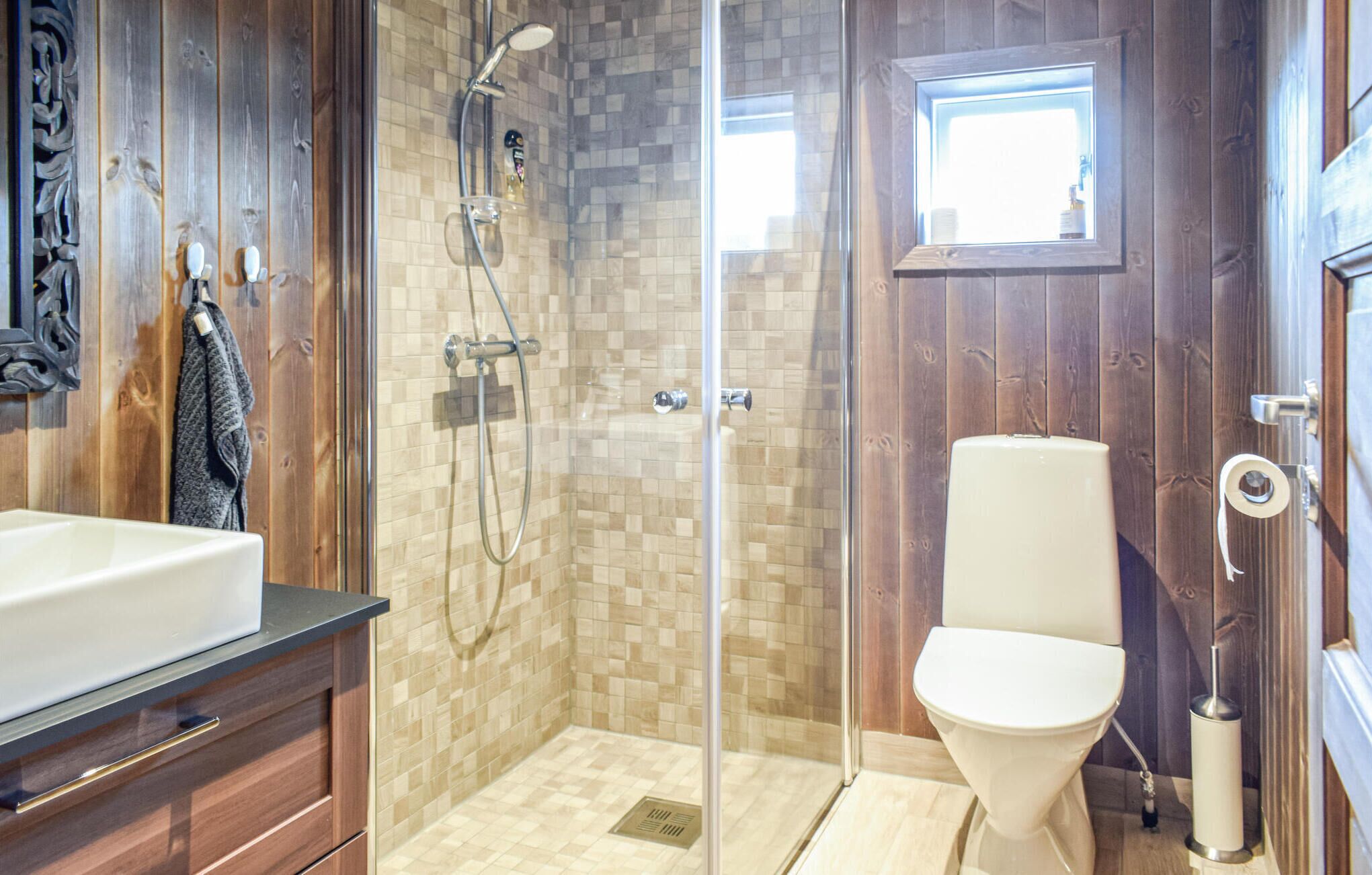Un bagno moderno con doccia vetrata, un water bianco e un mobile bagno in legno con lavandino.