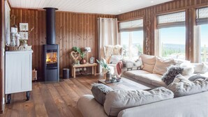 Un salón acogedor con chimenea, paredes de madera, un sofá y vistas al exterior.