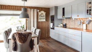 Una cocina moderna con paneles de madera, un comedor con una silla cubierta de piel y una lámpara colgante.