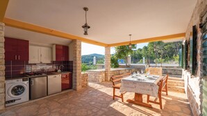 Una cocina con lavadora, un comedor con mesa y sillas, y vistas a zonas verdes y colinas.