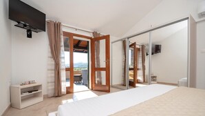 Un dormitorio con cama, televisor montado en la pared, puerta corrediza de vidrio que da a un balcón y una mesita de noche con lámpara.