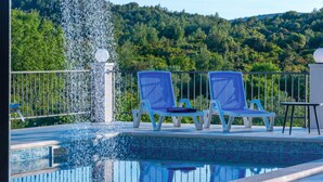 Zona de piscina con dos sillas reclinables azules, una mesita y una fuente.