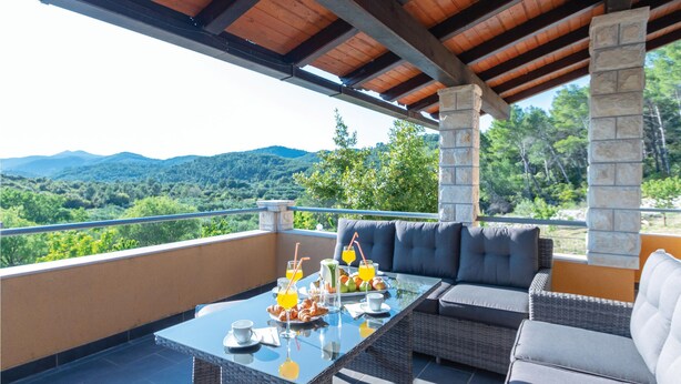 Un área de comedor al aire libre techada, con una mesa dispuesta para el desayuno, con vistas a un paisaje montañoso.