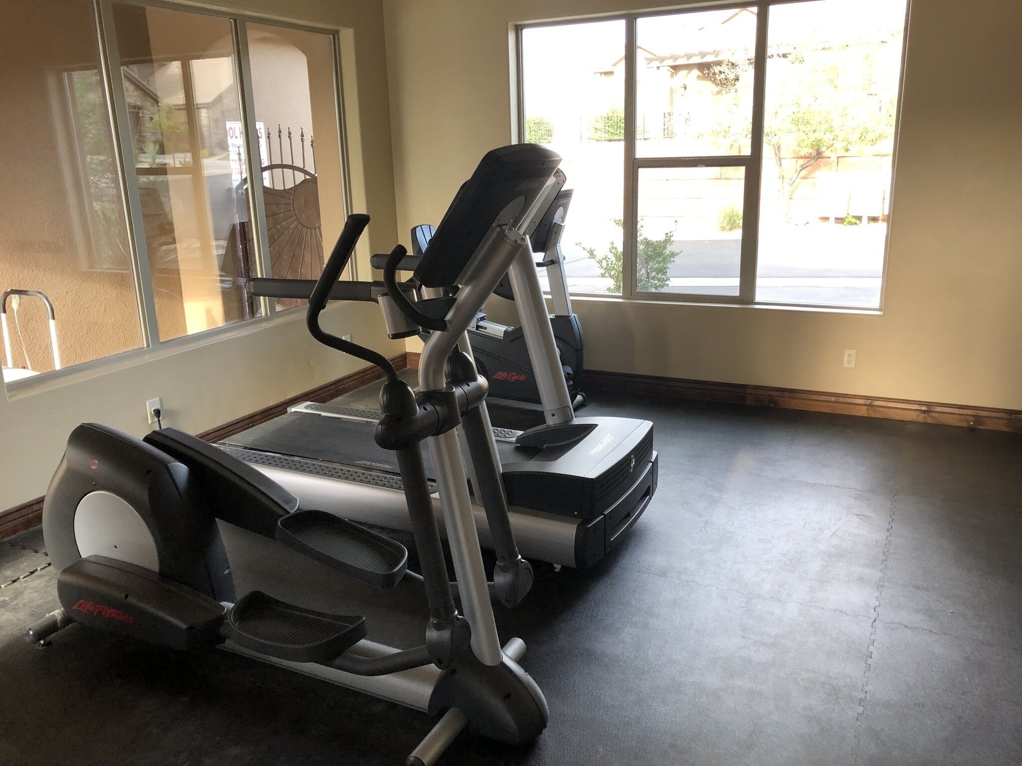 A gym with treadmills and a stationary bike, large windows, and a concrete floor.