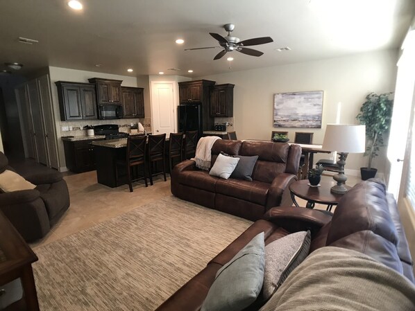 A modern living room with a brown leather sofa, a coffee table, and a rug. There is a kitchen area with dark wooden cabinets and a refrigerator. - Your home away from home! (Washington)