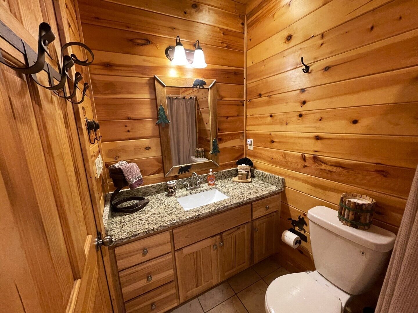 A wooden cabin bathroom with a granite countertop sink, wooden cabinets, a toilet, and a mirror with lights.
