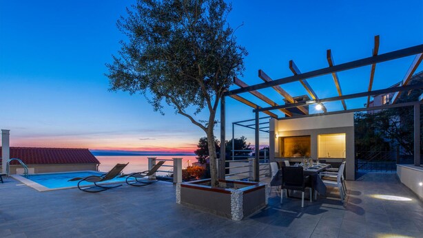 Un área de piscina en la azotea con sillones, una pérgola y una mesa de comedor con sillas.