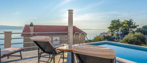 Zona junto a la piscina con sillones de descanso y vistas al agua y edificios.