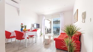 Una sala de estar moderna con un sofá rojo, una zona de comedor con sillas rojas, un televisor y un balcón con vistas.