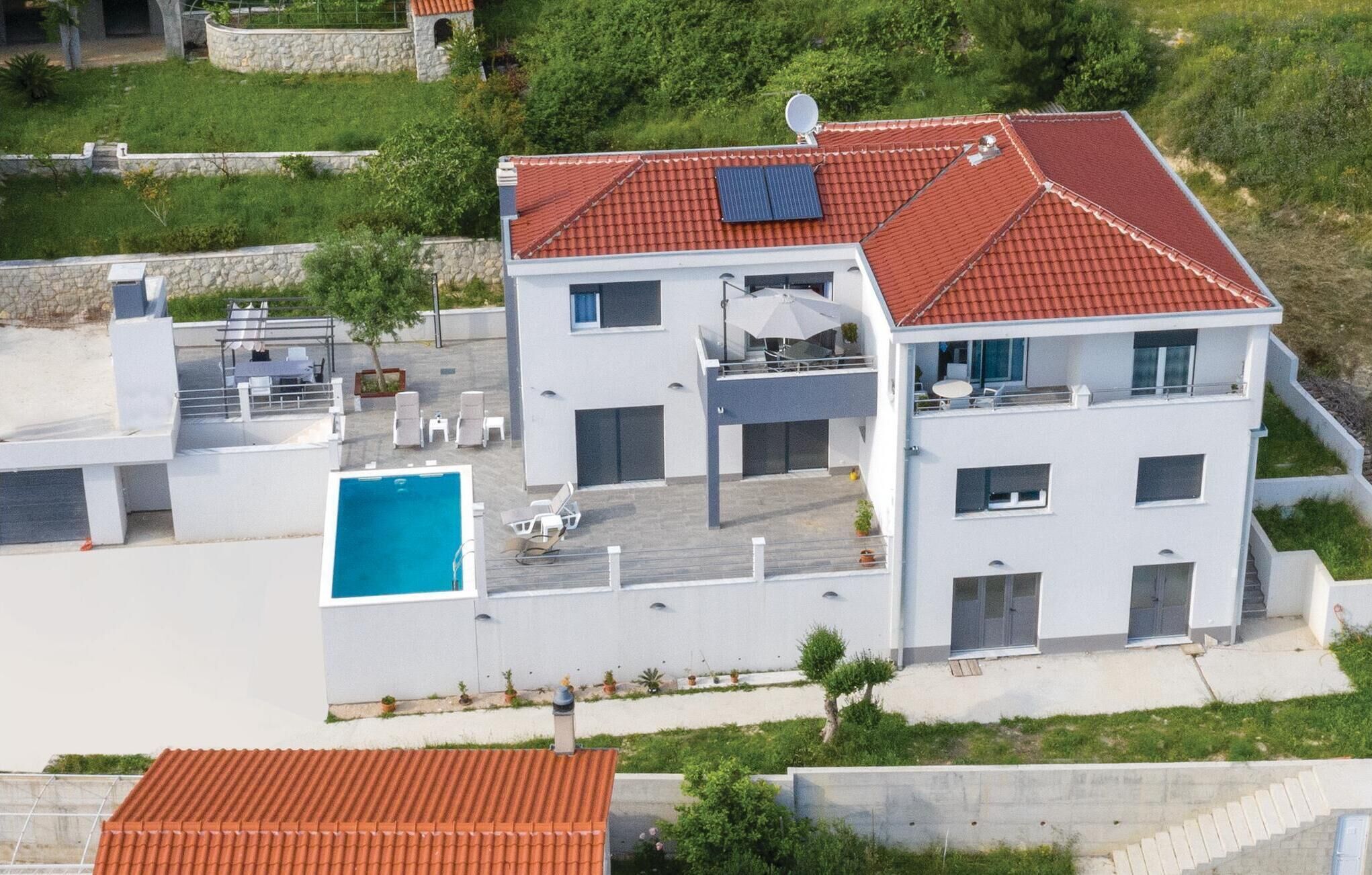 A modern two-story house with a red-tiled roof, a swimming pool, and a covered outdoor seating area.