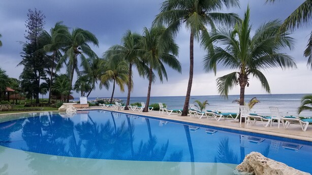 A swimming pool with lounge chairs, palm trees, and a view of the ocean. - Chac Hal Al, Casa Calandria lovely studio steps from the beach. (Puerto Aventuras)
