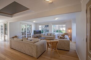 Relax in this spacious living room with a high ceiling and large windows, featuring a comfortable sofa set, flat-screen TV, and cozy reading nook.