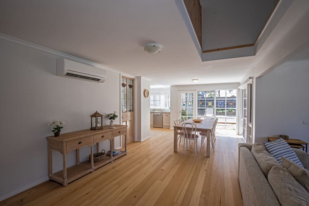 A spacious living area with a wooden floor, a dining table with chairs, a sofa, and a console table with decorative items.