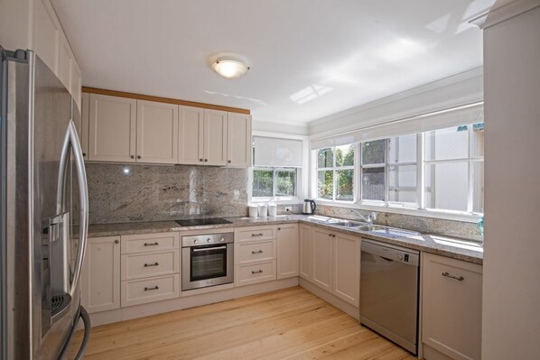 Enjoy cooking in this well-equipped kitchen with a refrigerator, oven, and dishwasher, set against a light-colored backdrop.