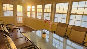 A sunlit room with a glass table, wicker chairs, and a view of the sea through large windows. - Soundfront with Gorgeous View and Private Pier! (Kill Devil Hills)