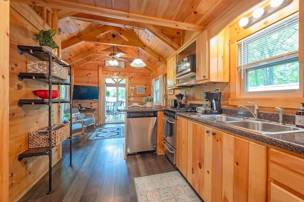 A wooden cabin interior with a kitchen, dining area, and a view of the outdoors.