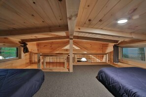 Una cabaña con techo alto, vigas de madera, una cama litera, una ventana y una pequeña mesa.