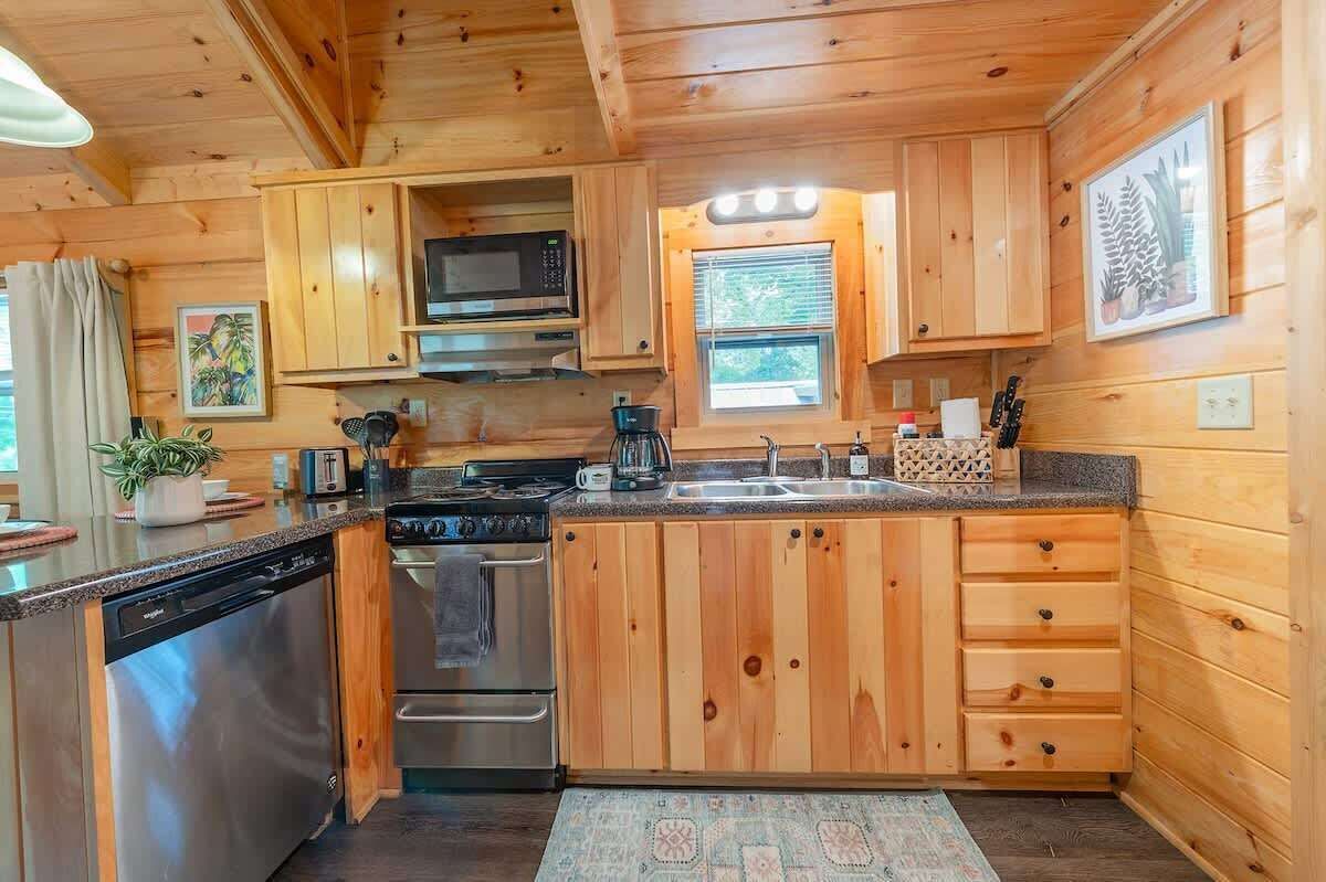 A wooden cabin kitchen with a dishwasher, stove, microwave, and sink.