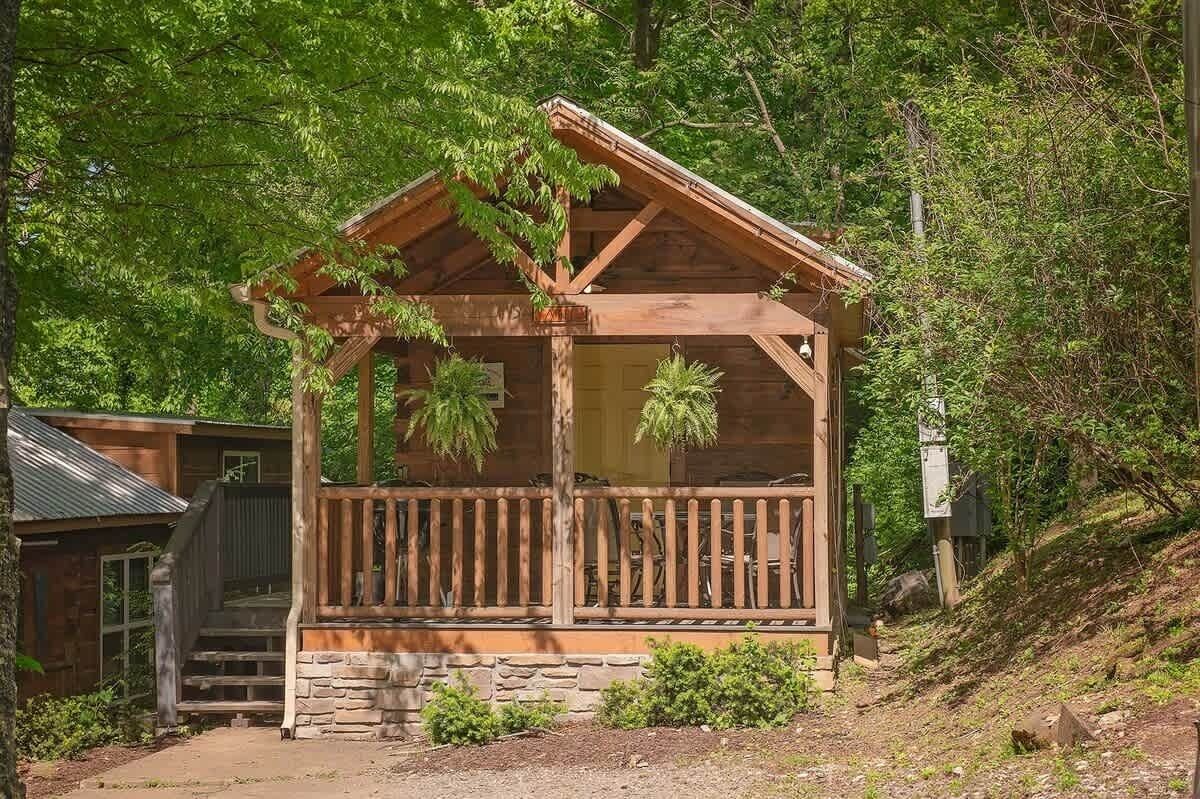 A wooden cabin with a porch, stone foundation, and surrounded by trees.