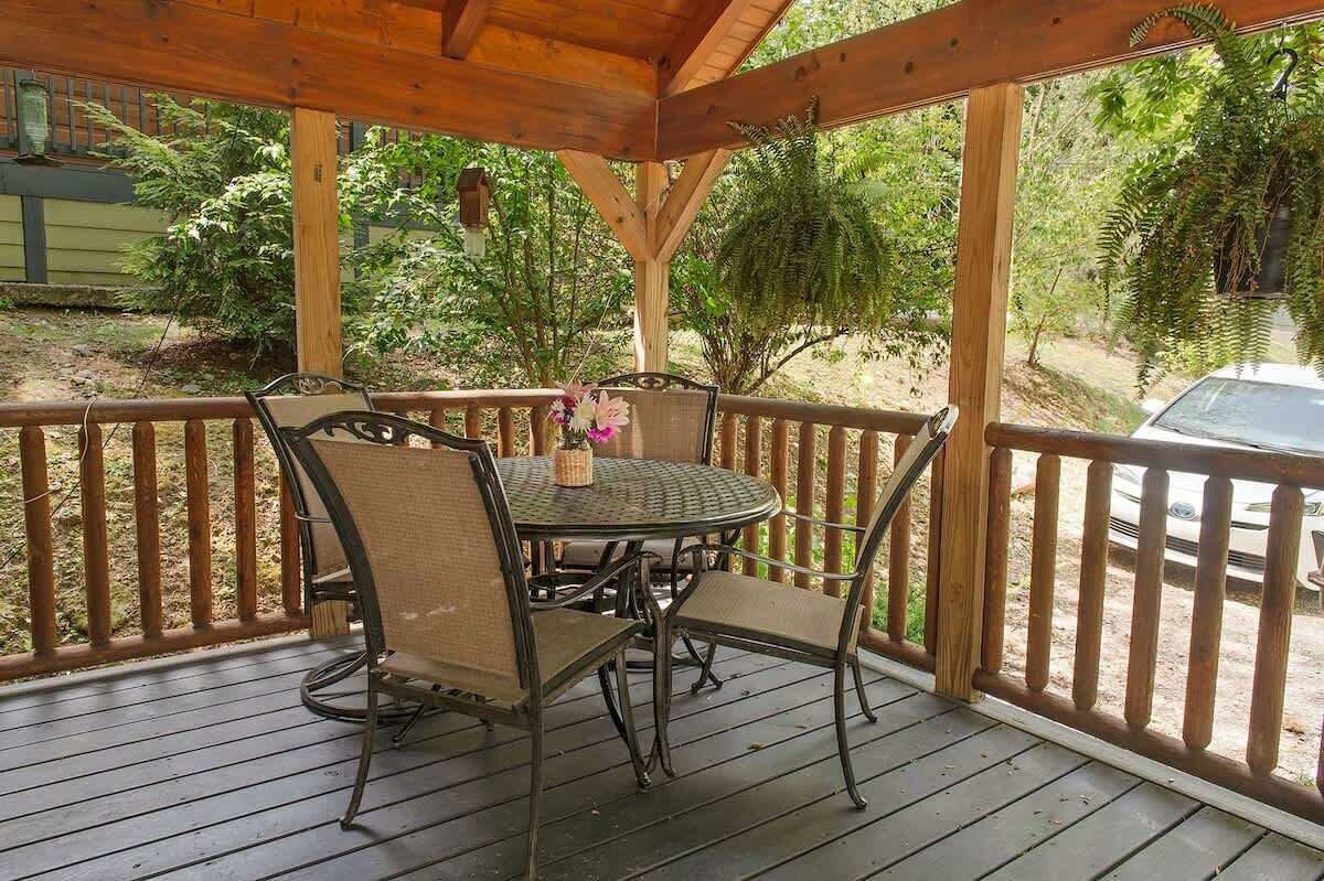 A covered outdoor patio with a round table and chairs, surrounded by a wooden railing.