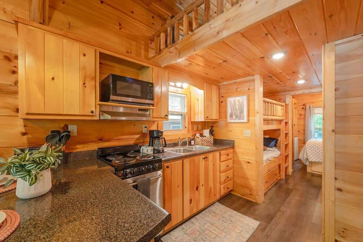 Interior de una cabaña con paredes de madera, una cocina con estufa, microondas y pileta.