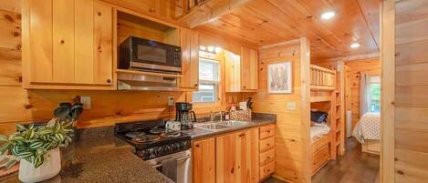 Interior de una cabaña con paredes de madera, una cocina con estufa, microondas y pileta.
