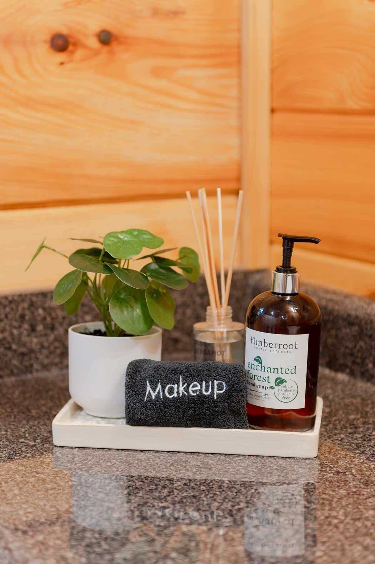 Een badkamermeubel met een potplant, een handdoek voor make-up, een fles Enchanted Forest zeep en rietstokjes voor een geurverspreider.