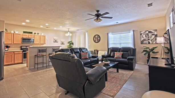 A modern living room with a sectional sofa, a coffee table, and a TV. There is a kitchen area with wooden cabinets and a microwave. - Near Airport, University, Stadiums & more. Sleeps 8 by a Premier Partner Host! (Albuquerque)