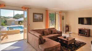 Una sala de estar con un sofá modular, una mesa de centro, un televisor de pantalla plana y un ventanal corredero que da a un balcón con piscina.