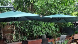 A wooden deck with outdoor furniture, including chairs and a table, under green umbrellas. - Self Contained Studio - Air-conditioned WiFi (Parramatta Park)