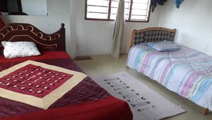Een kamer met twee bedden, waarvan één met een rode sprei en de andere met een gestreepte sprei. Op de vloer ligt een quilt en er is een raam met gordijnen.