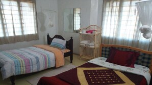 Een slaapkamer met twee eenpersoonsbedden, een houten babybedje, een spiegel en een raam met gordijnen.