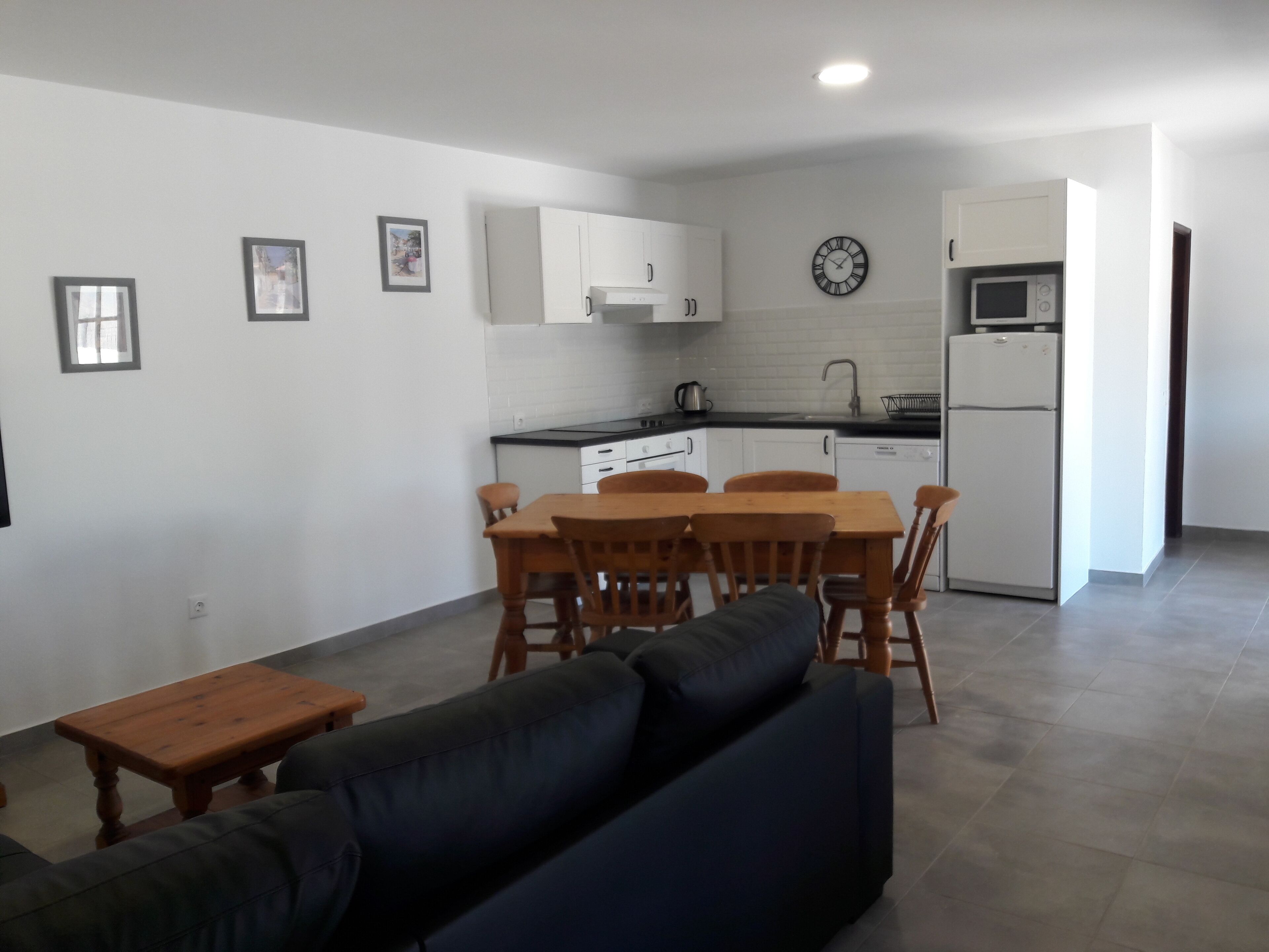A modern kitchen with white cabinets, a microwave, and a dishwasher. There is a dining area with a wooden table and chairs.